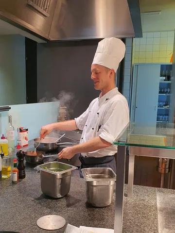 Joshua Bloch in weisser Kochjacke und Kochmütze bereitet an der Live-Cooking-Station eine Sauce zu — Koch EFZ und Sous-Chef aus Olten bei der Arbeit am Herd.